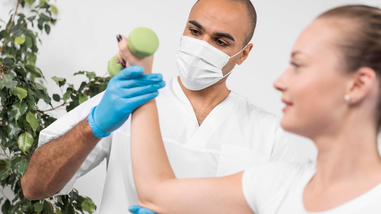 Chiropractor wearing medical mask assessing woman’s muscle strength during care