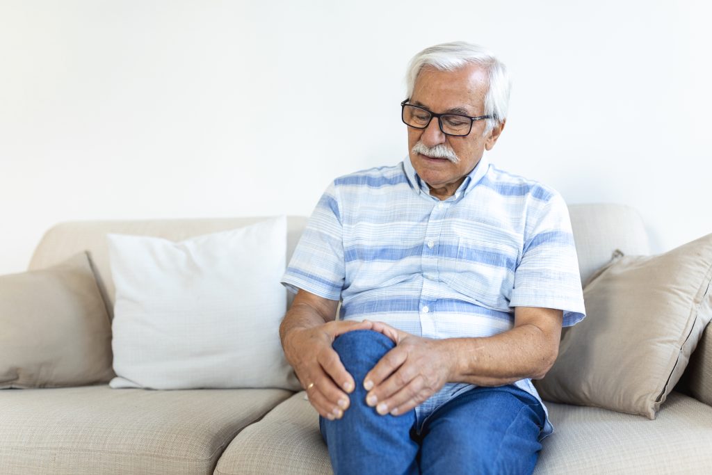 Man sitting on a sofa at home, holding his knee in discomfort
