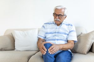 Man sitting on a sofa at home, holding his knee in discomfort