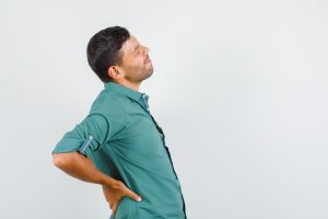 Young man suffering from back pain in shirt.